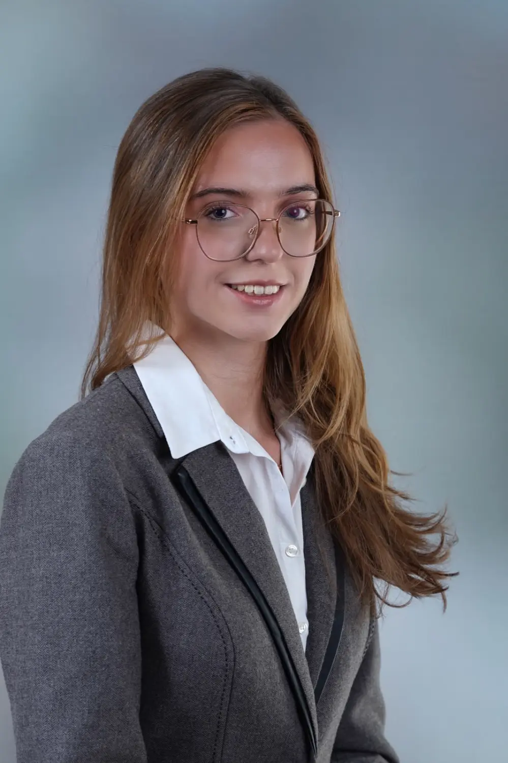 Bewerbungsfoto einer jungen Frau mit Brille vor blaugrauem Studiohintergrund